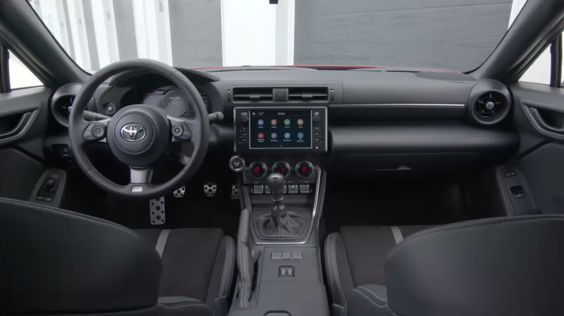 Toyota GR86 2026 interior showing simple driver-focused cabin physical climate control buttons tight-holding sport seats standard Apple CarPlay smartphone integration and premium fuel requirement for best performance