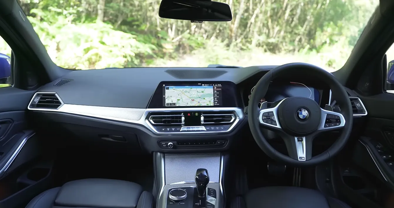 BMW 330i 2026 interior showing 14.9 inch curved iDrive screen faster and cleaner than rivals tight sport seats that hug through corners wireless charging adaptive cruise standard and crisp button layout that keeps driver focus
