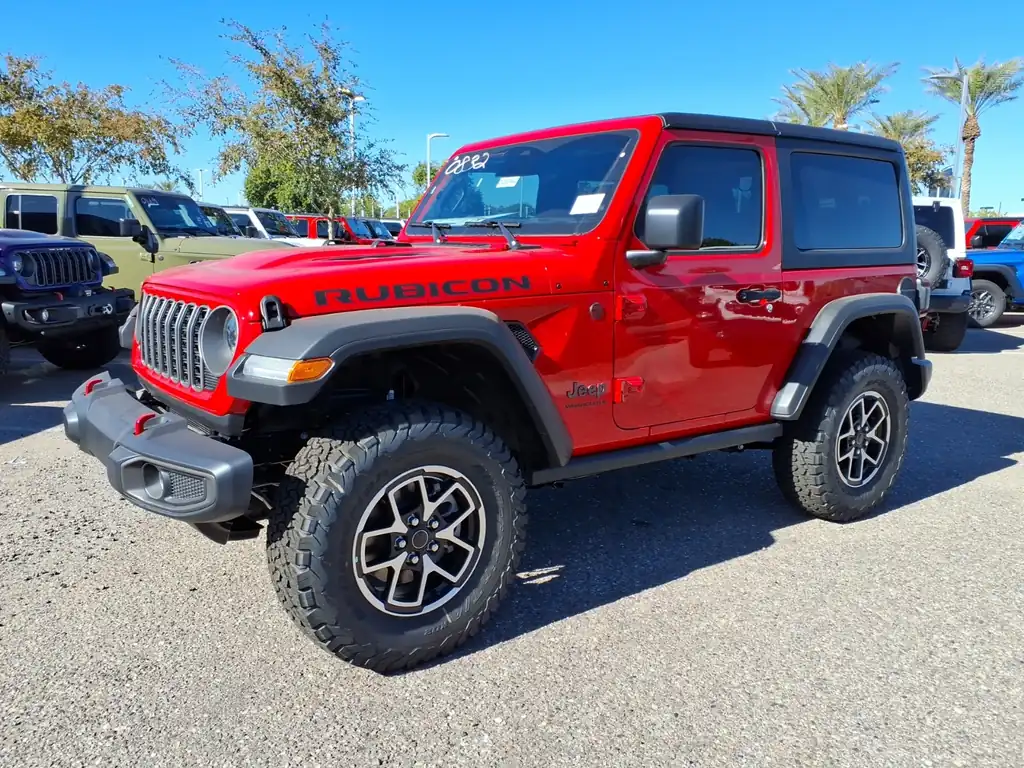 Red 2026 Jeep Wrangler Rubicon 2-door with a black hardtop and all-terrain tires on a dealer lot