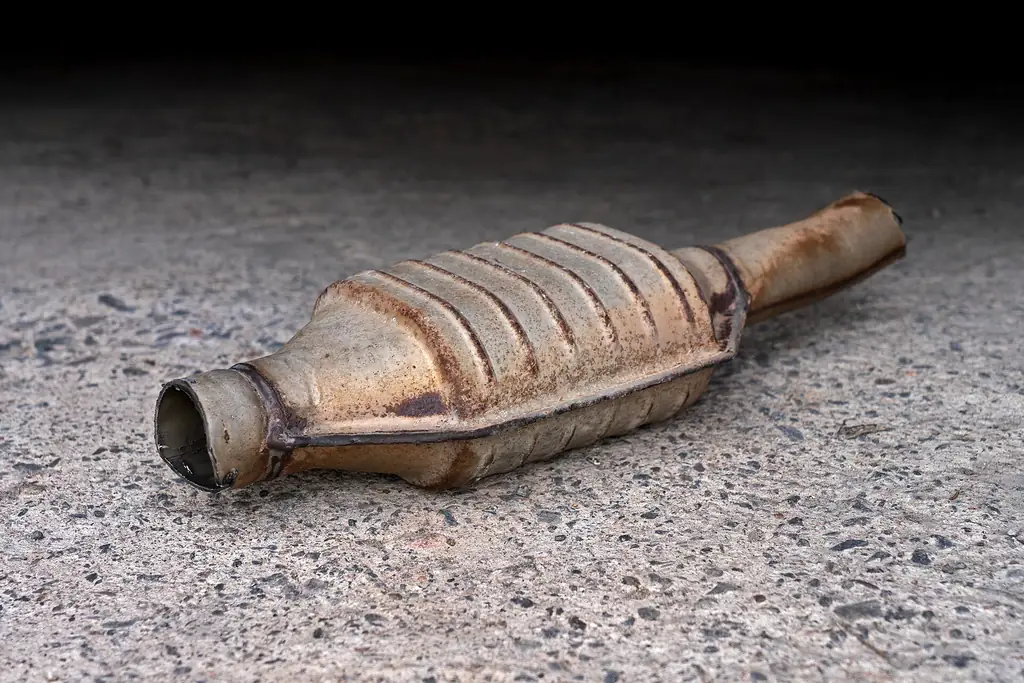 A rusty used automotive catalytic converter lying on a concrete floor