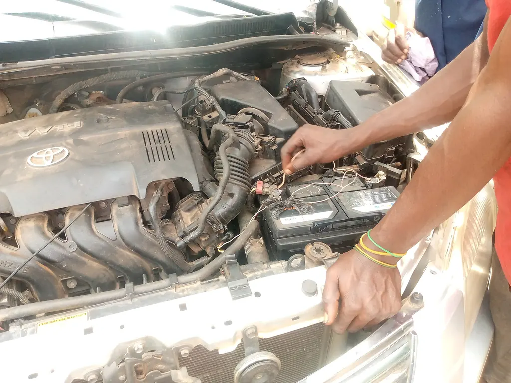Mechanic working at the 12-volt battery in the engine bay of a Toyota with a VVT-i four-cylinder engine