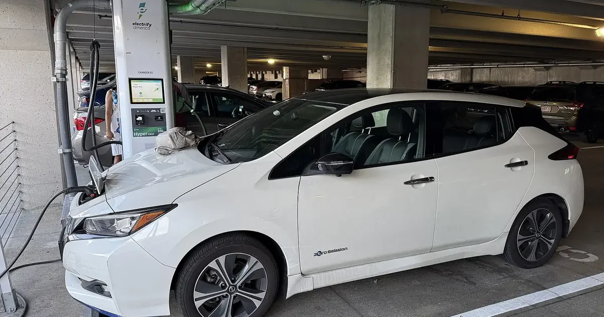 White Nissan Leaf plugged into a public charging station inside a parking garage