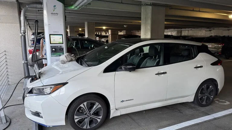 White Nissan Leaf plugged into a public charging station inside a parking garage