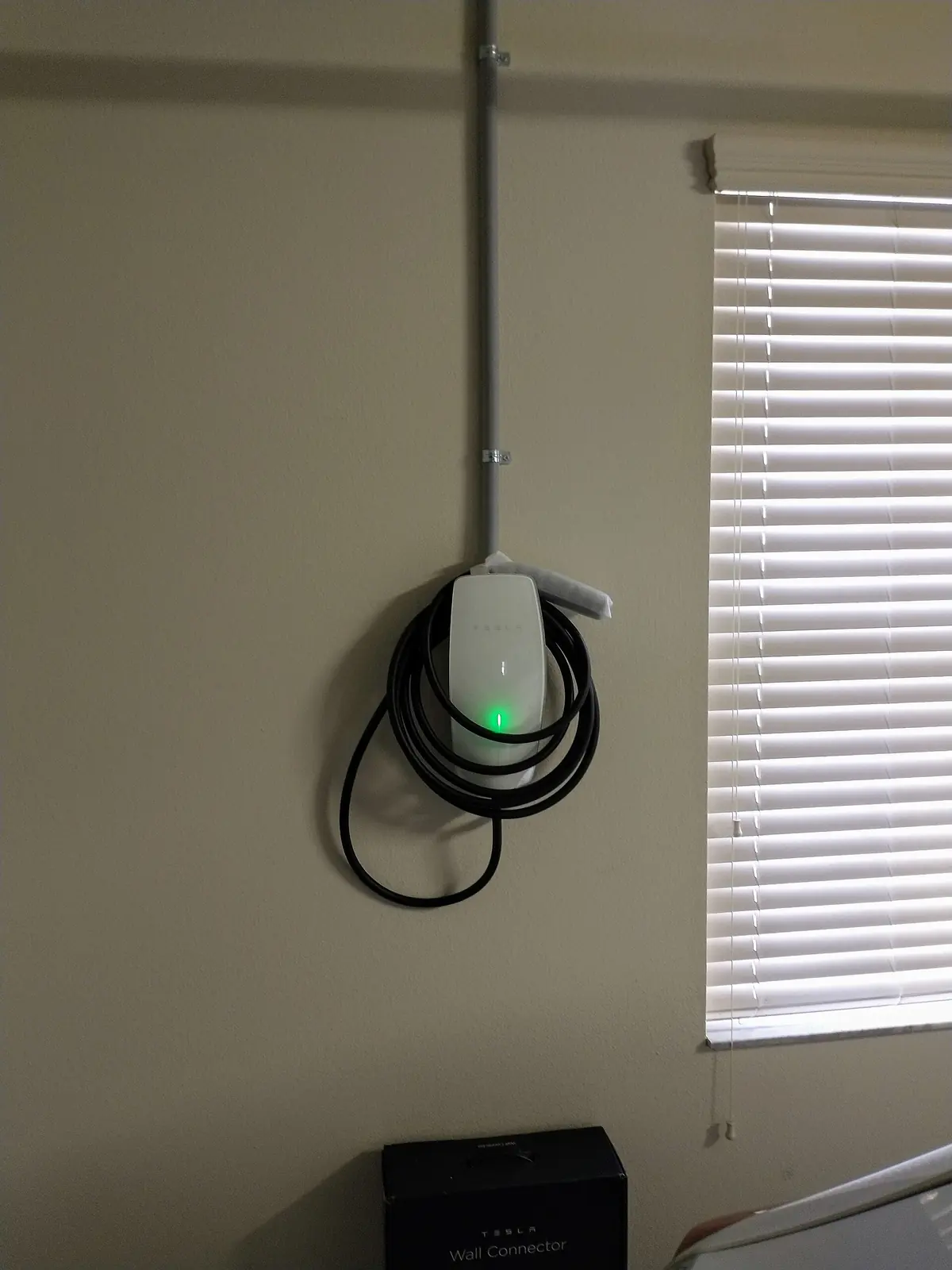 Tesla Wall Connector with its cable coiled, mounted on an interior wall with conduit running to the ceiling