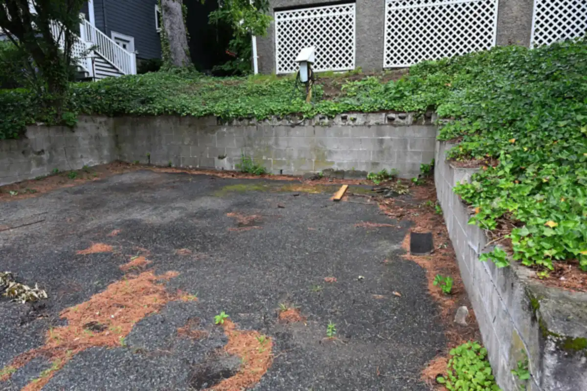Wall-mounted home EV charger installed outdoors on a retaining wall beside a residential parking pad