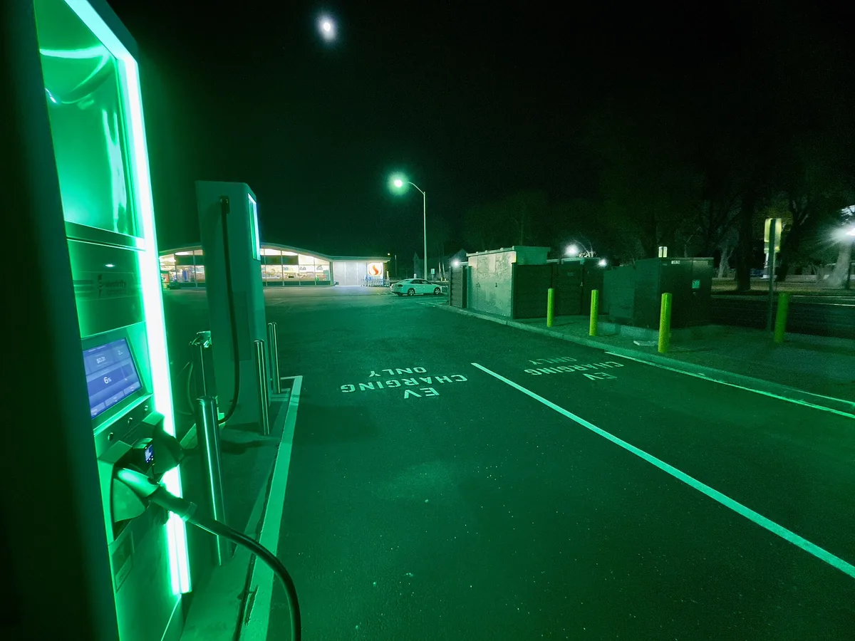 Electrify America DC fast charger lit in green at a Safeway parking lot at night