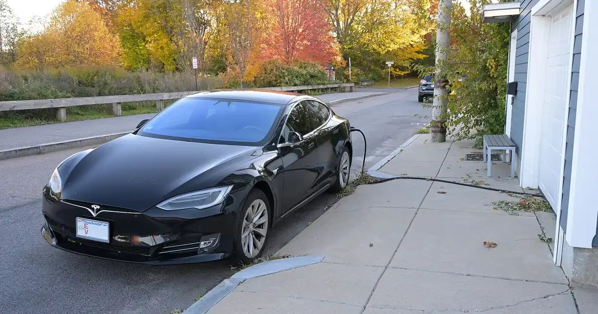 Black Tesla Model S parked at a curb and plugged into a charger at a home in Dorchester, Boston