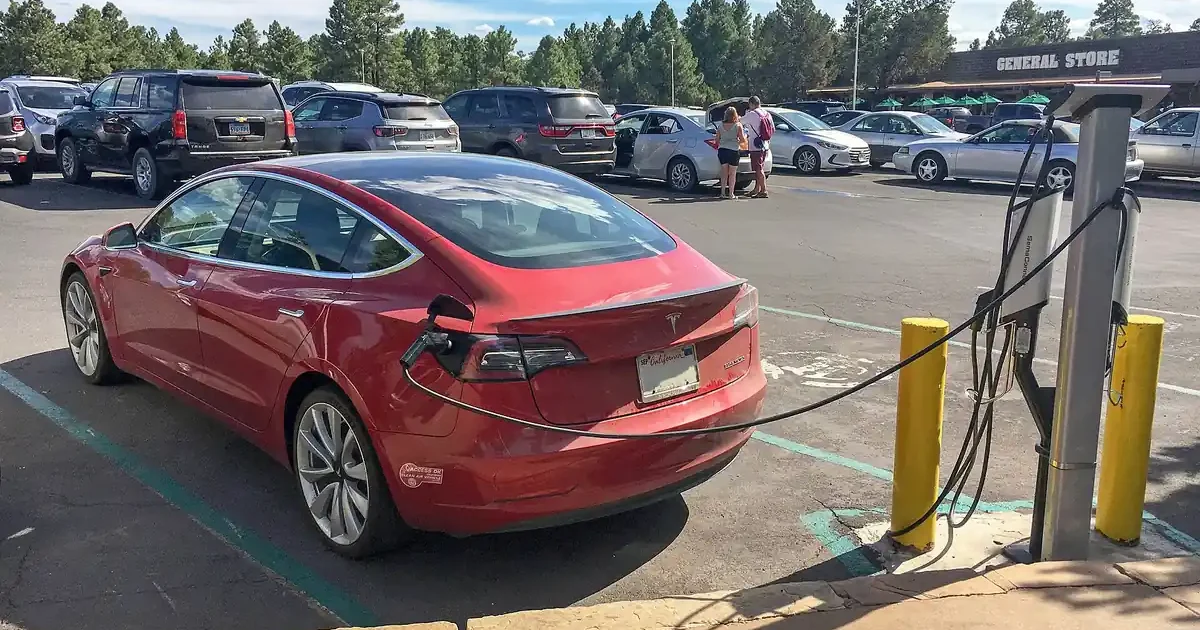 Red Tesla Model 3 plugged into a Level 2 charging station in a lodge parking lot at Grand Canyon National Park