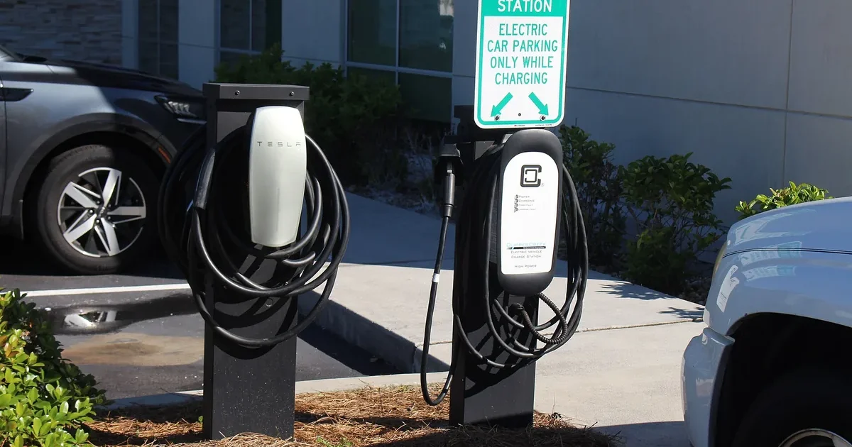 Two Level 2 EV charging pedestals with J1772 cables beside a hotel parking space marked for electric car charging