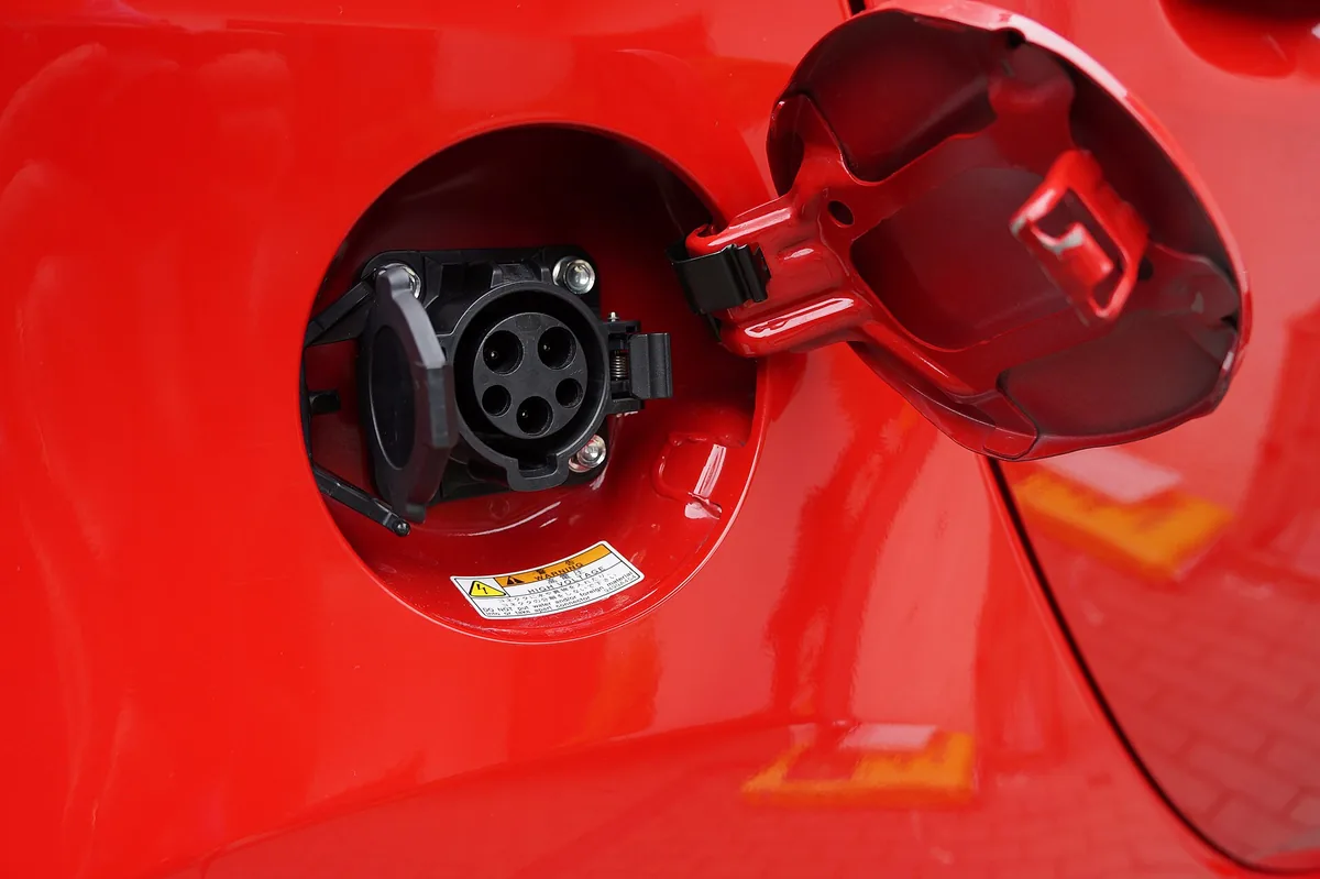 Open charge port door on a red electric car showing the round SAE J1772 Level 2 AC charging inlet