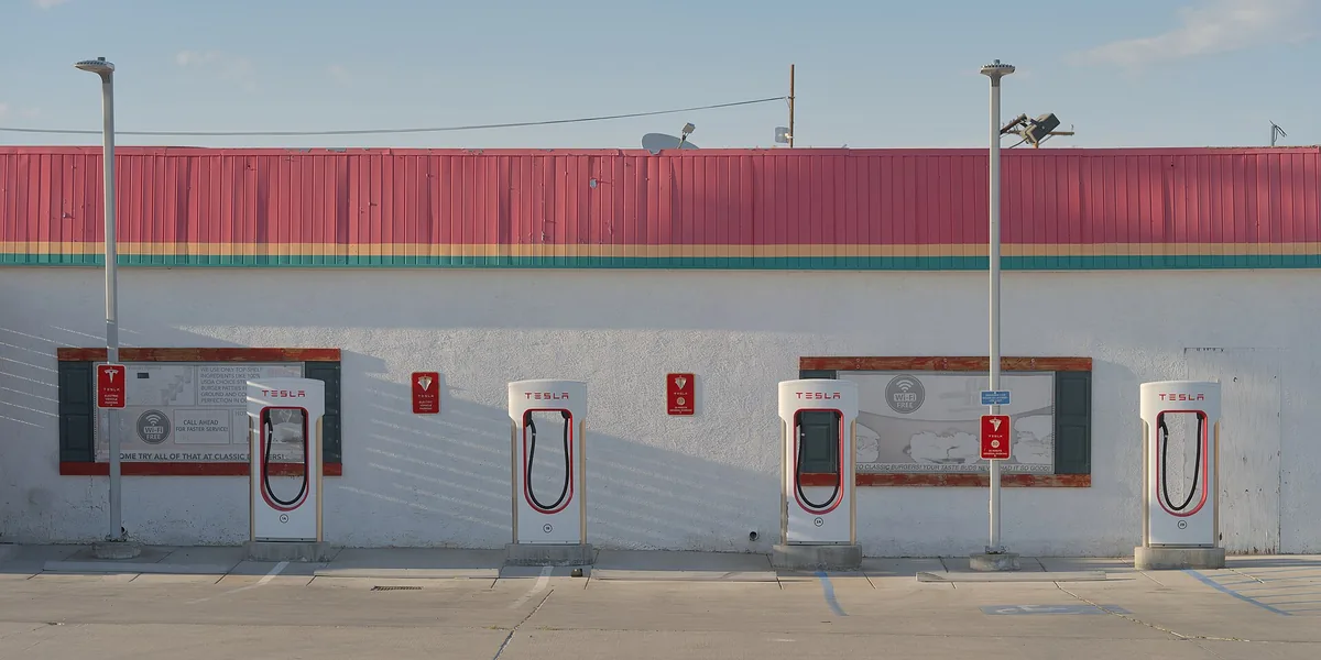 Row of red-and-white Tesla Supercharger stalls along a wall in Inyokern, California