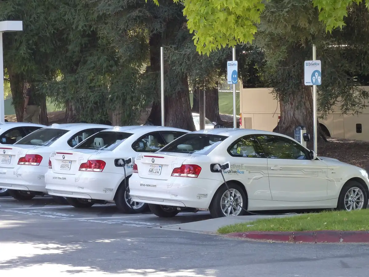 Row of white BMW electric cars plugged into workplace Level 2 chargers in a corporate parking lot