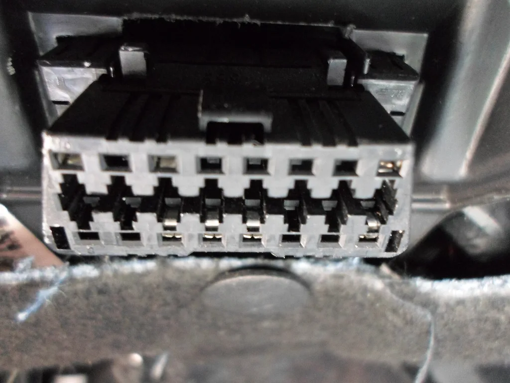 Close-up of a 16-pin OBD-II diagnostic connector mounted under a car dashboard