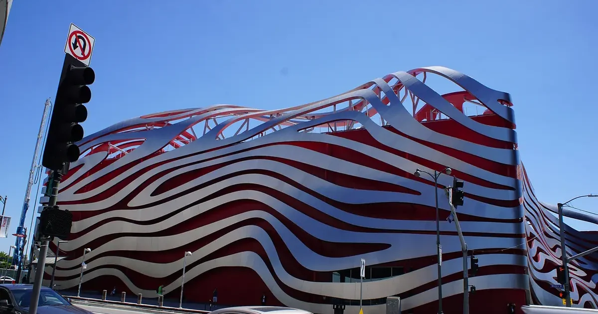 Exterior of the Petersen Automotive Museum on Wilshire Boulevard in Los Angeles, with its red facade wrapped in curving stainless steel ribbons