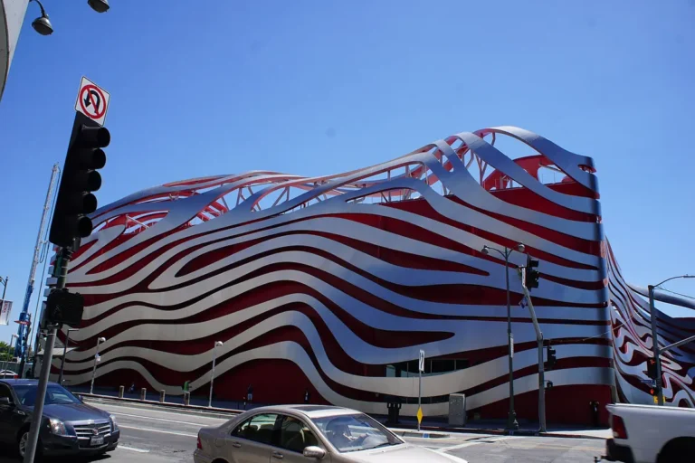 Exterior of the Petersen Automotive Museum on Wilshire Boulevard in Los Angeles, with its red facade wrapped in curving stainless steel ribbons