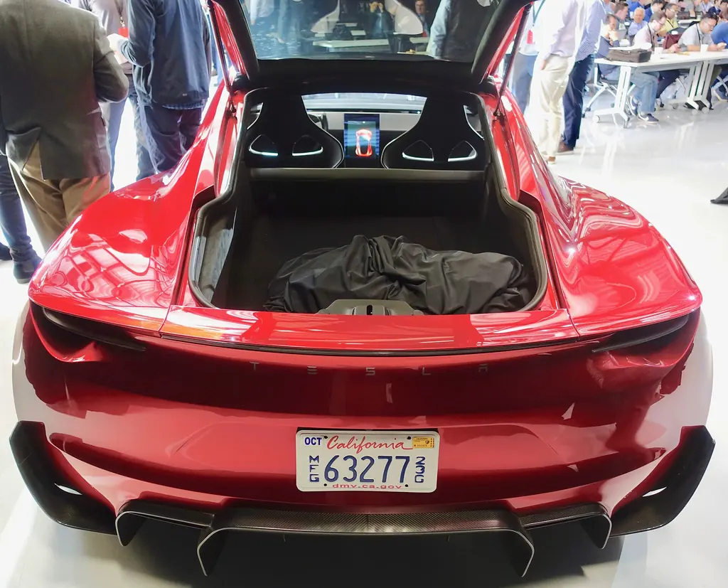 Rear view of a red Tesla Roadster prototype with the rear hatch open showing the cargo area and seats