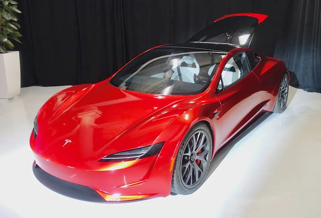 Red Tesla Roadster prototype with its removable glass roof panel lifted, displayed indoors against black curtains